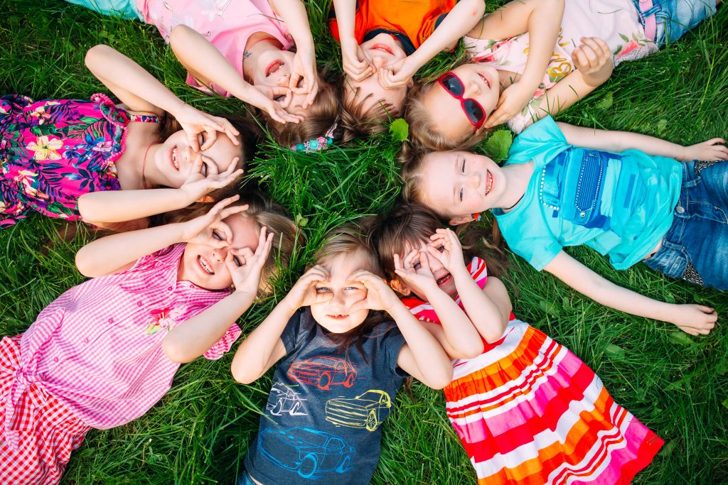 Kids are lying on the glass to form a circle, they’re looking at the sky happily and form a glasses by their hands