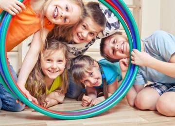 There are five kids who want to look through the circle ring. They are happy and smiling.